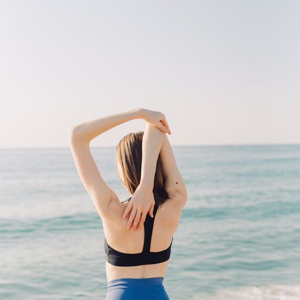 Person feeling energized and stretching outdoors with the sun behind them.
